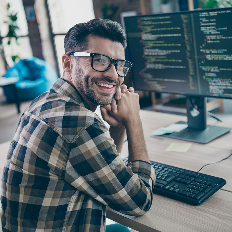 Man sitting at a desk with computer monitors and keyboard, smiling.