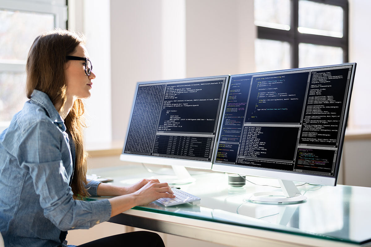 Person working at a desk with three computer monitors displaying code.