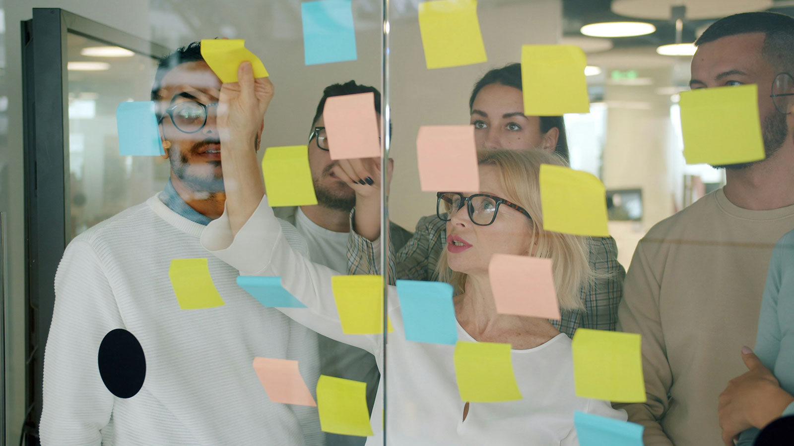 Group of people brainstorming with colorful sticky notes on a glass wall.